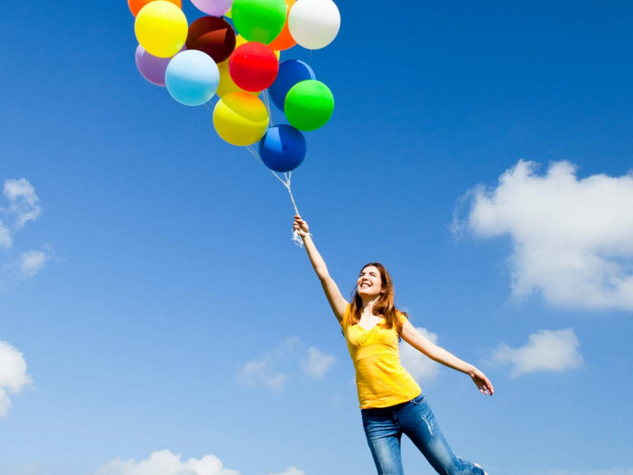 Woman holding onto balloons flying in the sky.