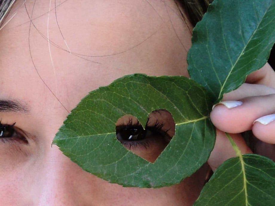 A woman looking through a heart-shaped hole in a leaf.