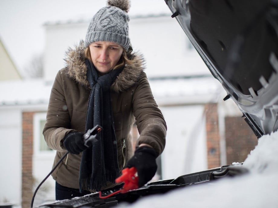 Woman in winter clothing trying to jumpstart her car in the cold.