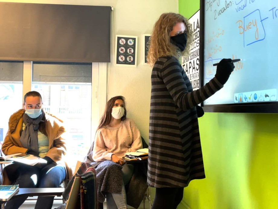 teacher in mask writing on whiteboard while students look on.