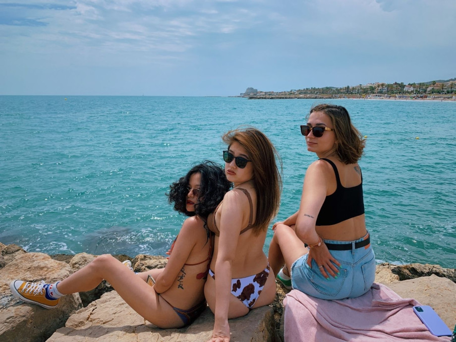3 stylish ladies sitting on a rock by the blue sea.