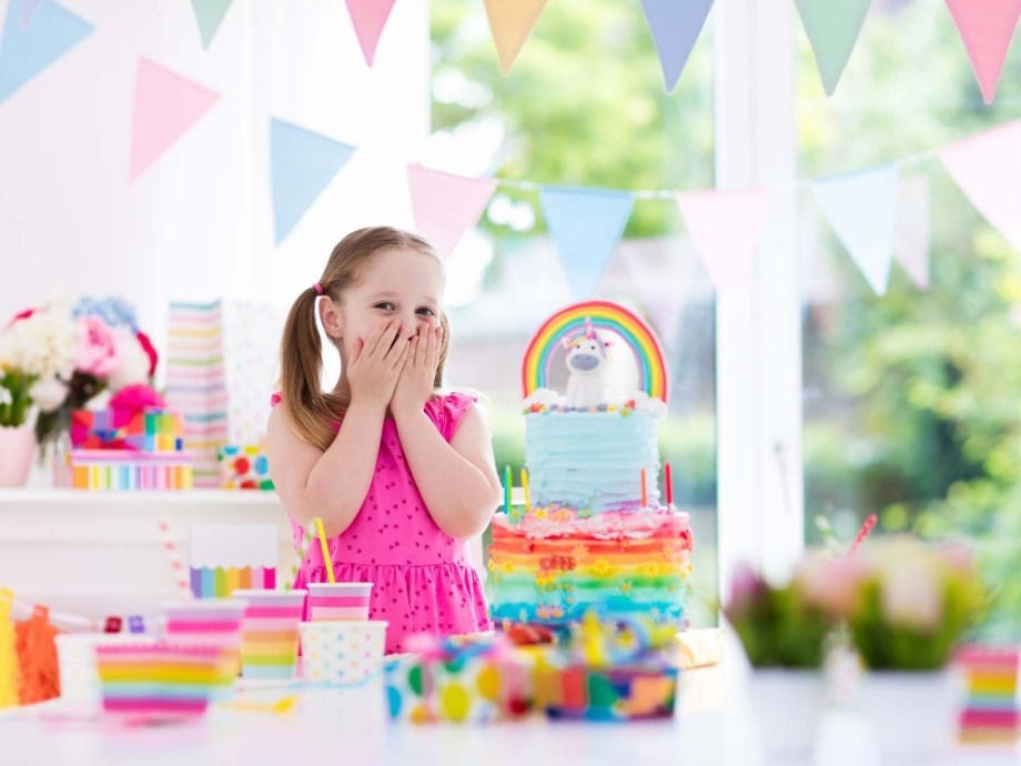 Girl in front of a birthday cake covering her mouth in surprise.