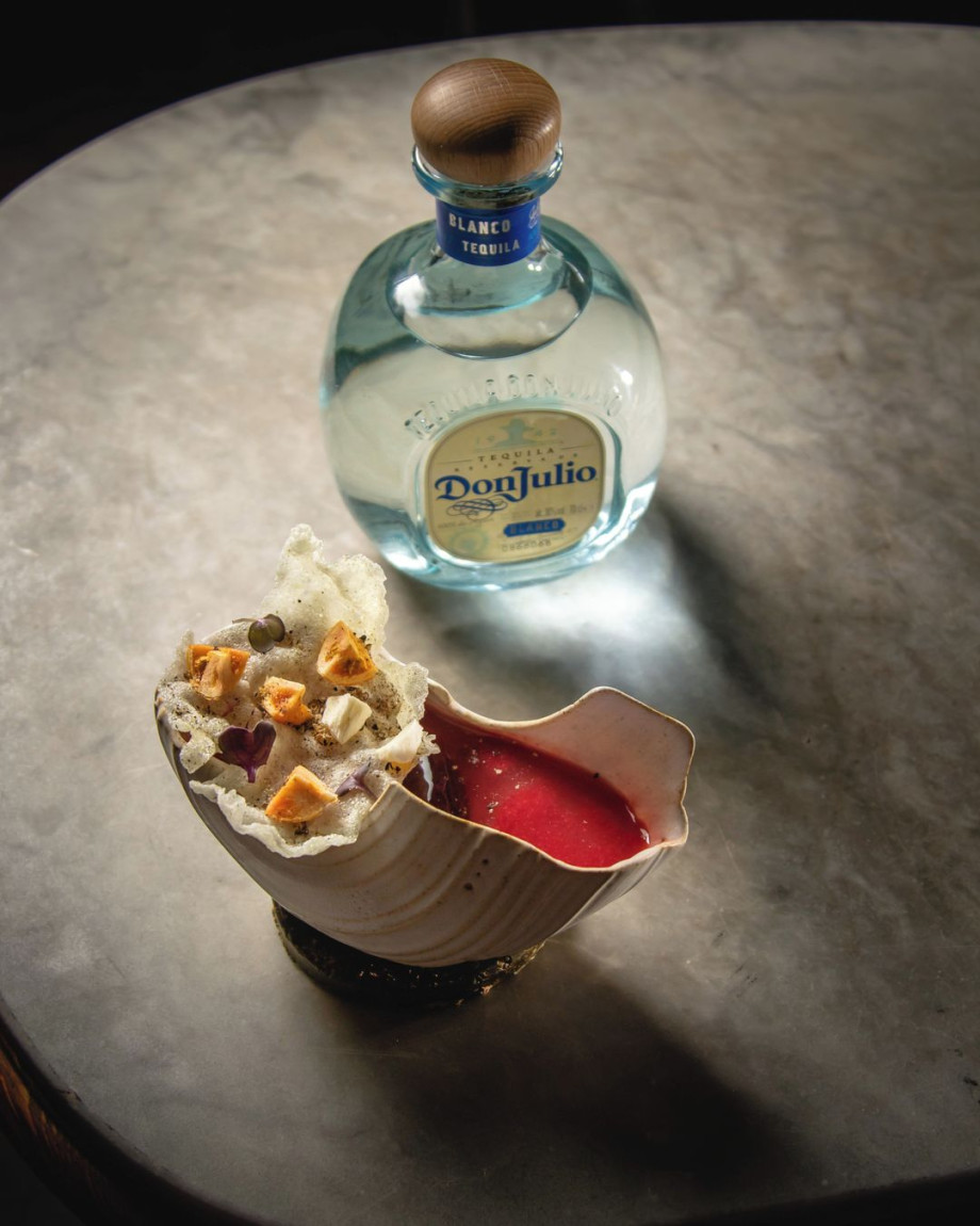 Cocktail in a conch next to bottle of Don Julio tequilia.