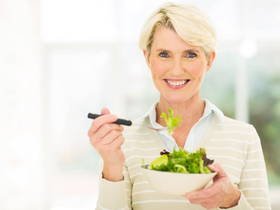 Smiling woman eating salad.