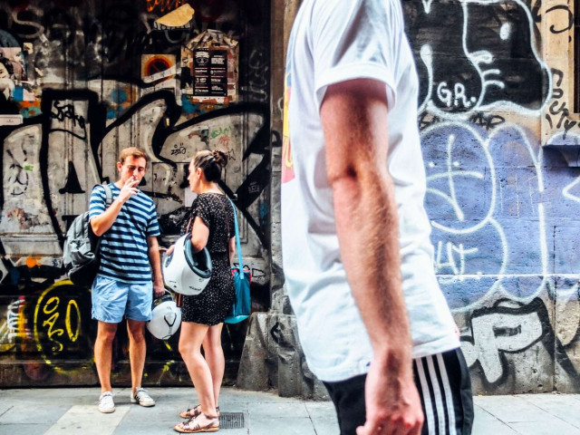 two friends talking and smoking in Gothic Quarter in Barcelona with man in sports clothes walking by