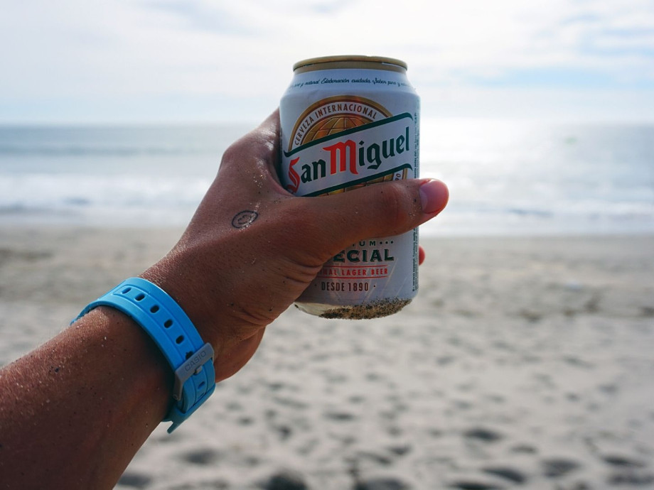 Hand holding can of San Miguel beer in front of the beach.