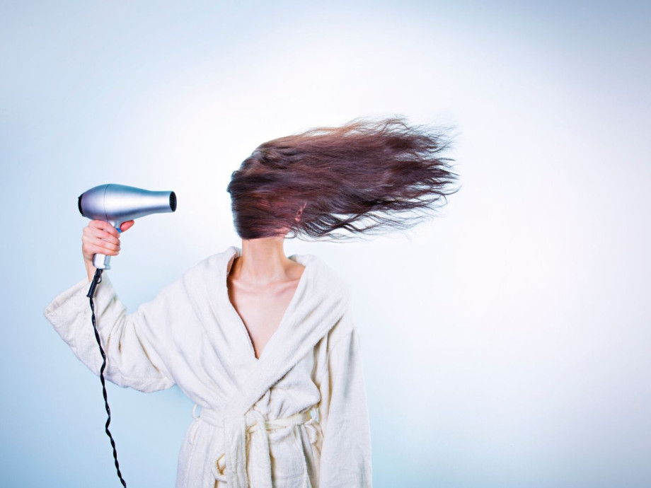 Lady holding hairdryer to the side of her head while her hair flies in one direction across her face.