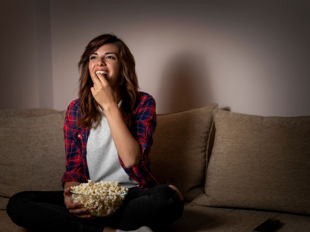 Girl sitting on couch eating popcorn in front of TV