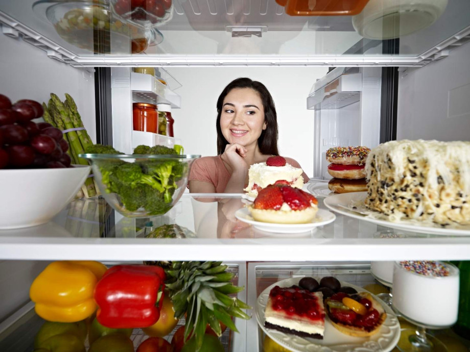 A woman looking in the fridge and eyeing the desserts.