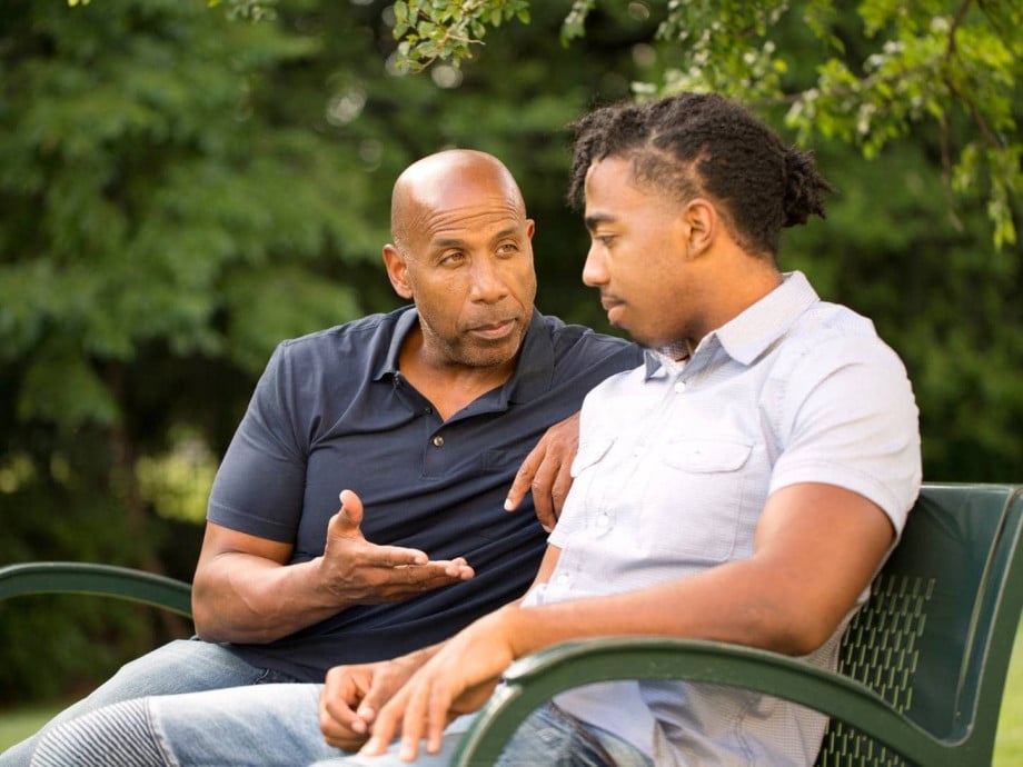 Father giving advice to son on bench in park.
