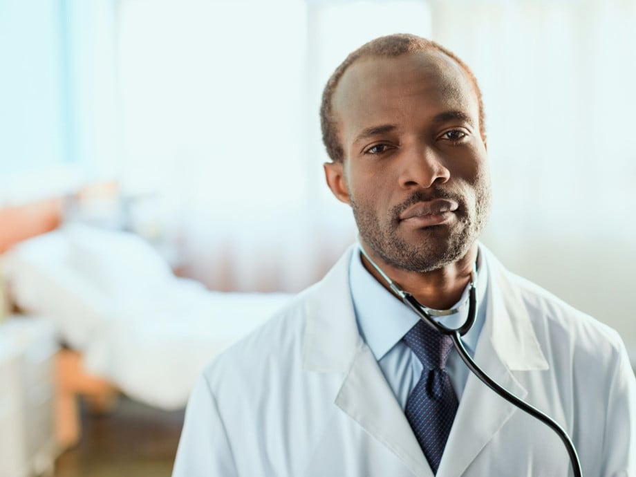Doctor in lab coat standing in front of hospital bed.